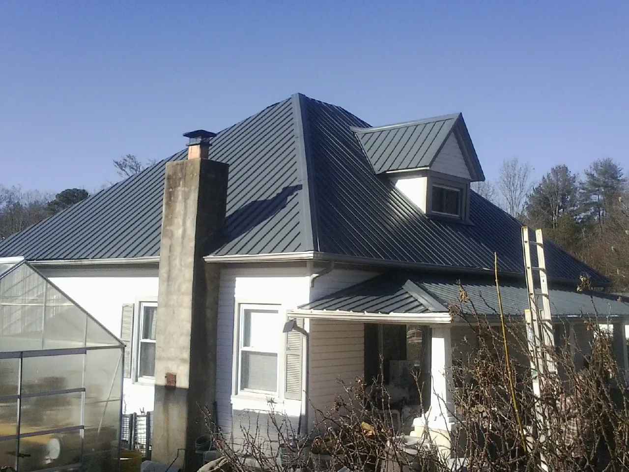 Dark blue standing seam metal roof on a white farmhouse with dormer — Slate & Tile Roof Repair by Roofing Brothers in Marina