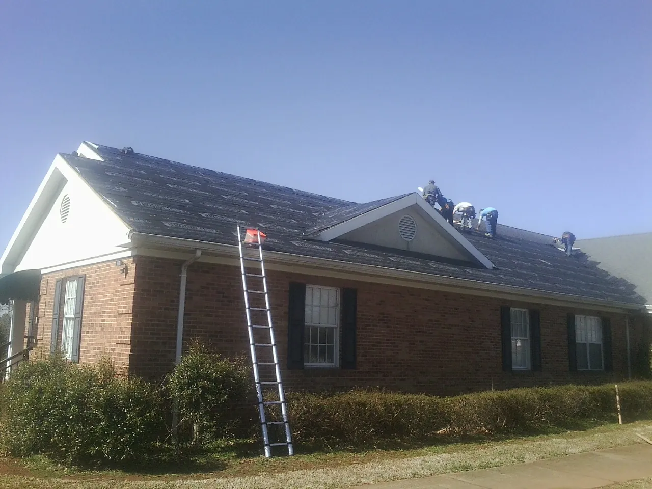 Crew tearing shingles off a brick ranch roof with a ladder set — Metal Roof Repair work by our crew in Marina