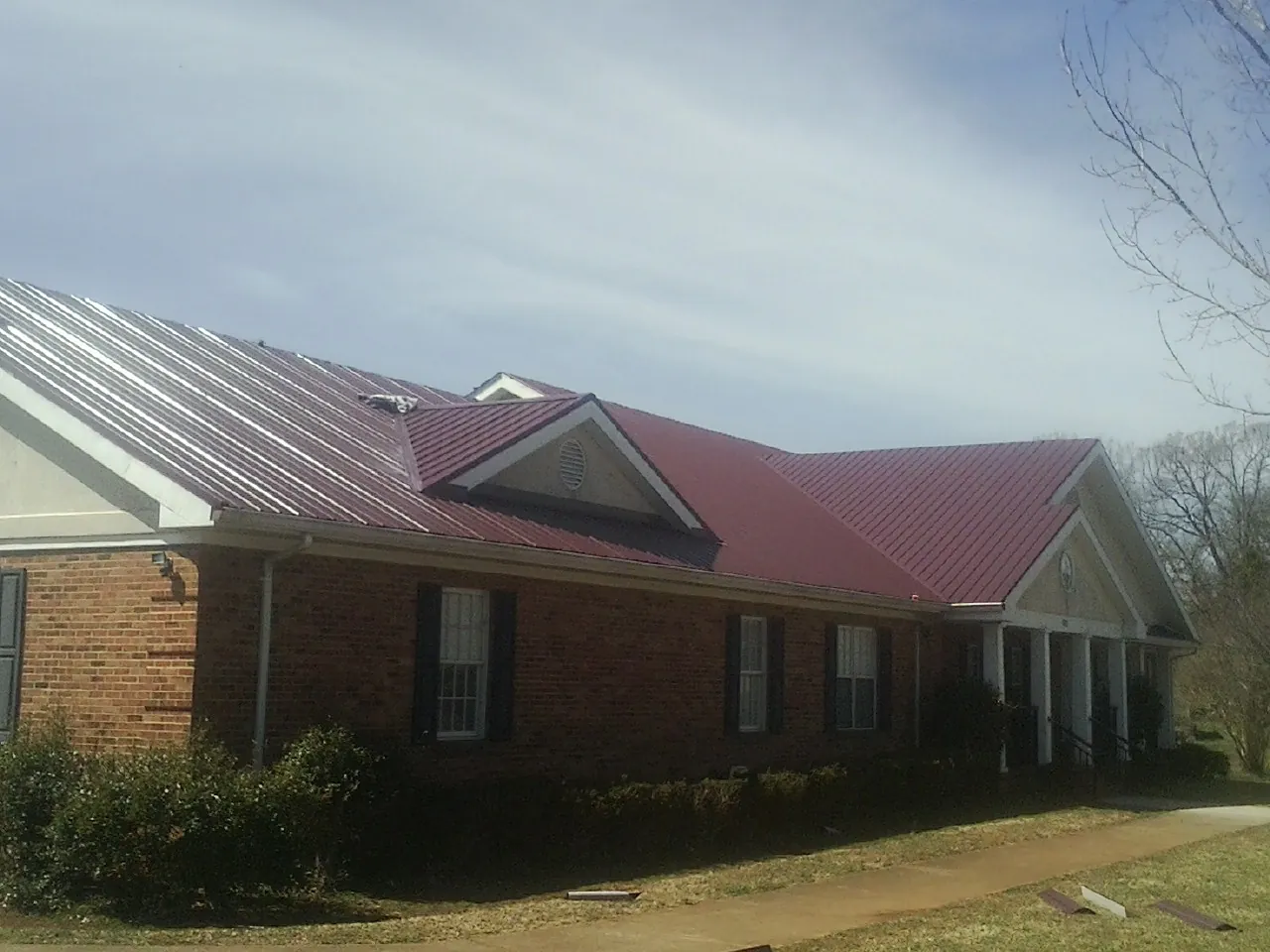 Red metal roof with gabled entries on a long brick building, from a Hail Damage Roof Repair job in Marina