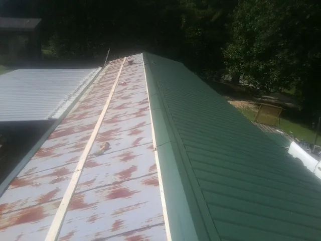 Old rusted panels beside newly installed green metal roofing — Wind Damage Roof Repair by Roofing Brothers in Marina