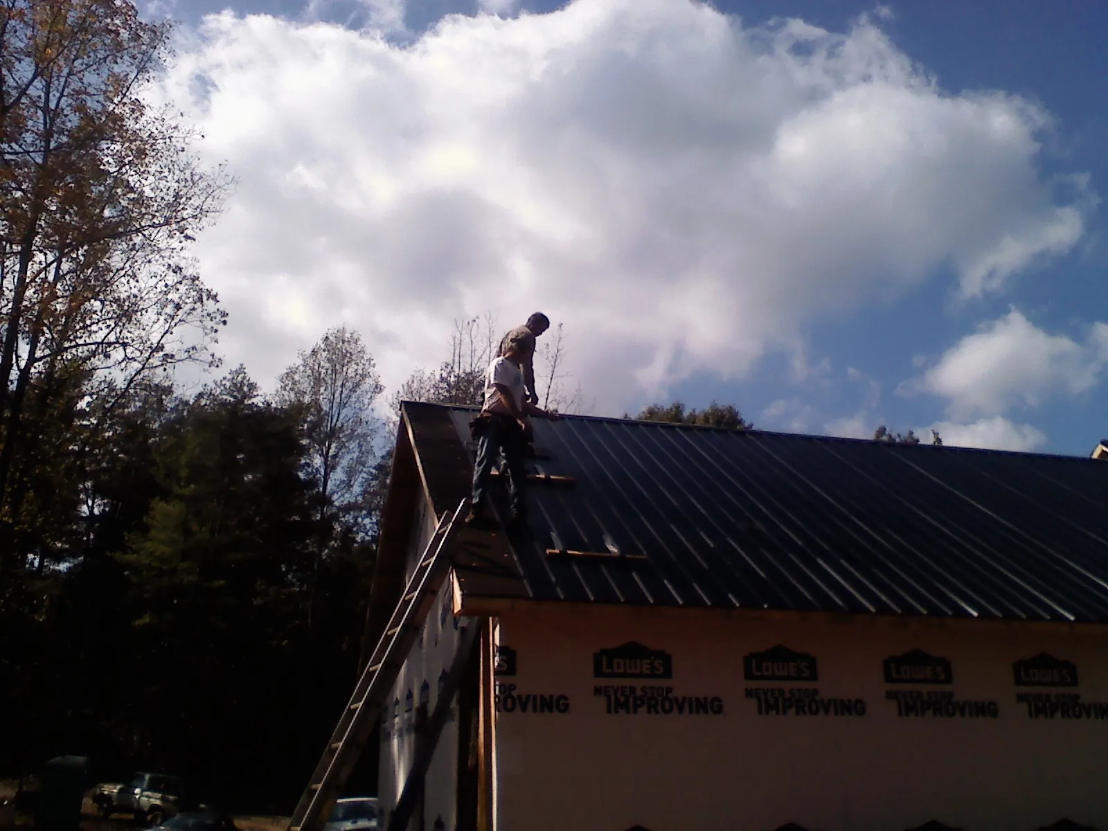 Roofer fastening dark metal panels high against a cloudy sky, from a Roof Inspection job in Marina